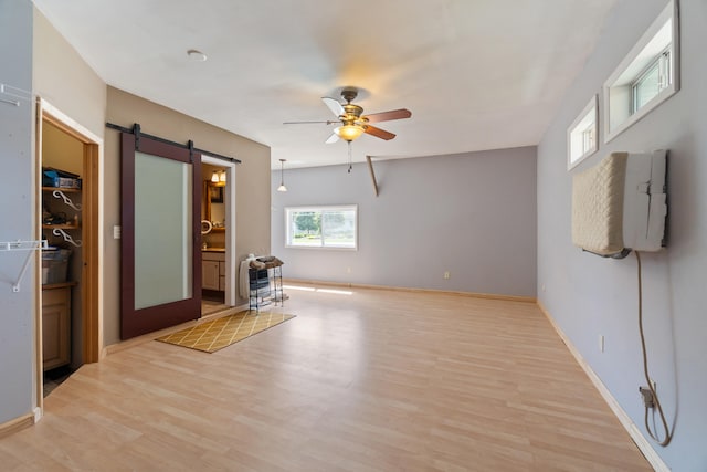 unfurnished room featuring a barn door, ceiling fan, and light hardwood / wood-style floors