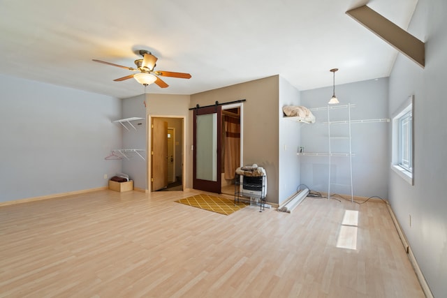 spare room featuring light wood-type flooring, a barn door, heating unit, and ceiling fan