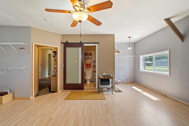 unfurnished living room with a barn door, ceiling fan, heating unit, and light wood-type flooring