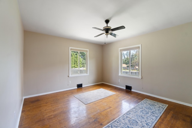 empty room featuring plenty of natural light, ceiling fan, and dark hardwood / wood-style flooring