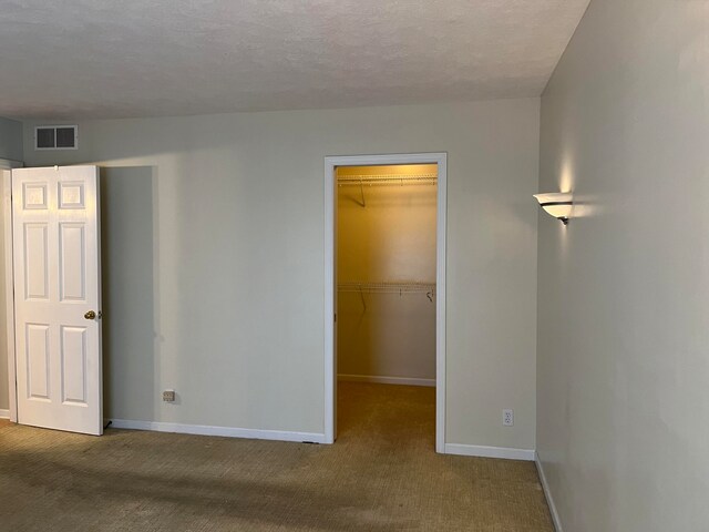 unfurnished bedroom with a spacious closet, visible vents, baseboards, and carpet floors