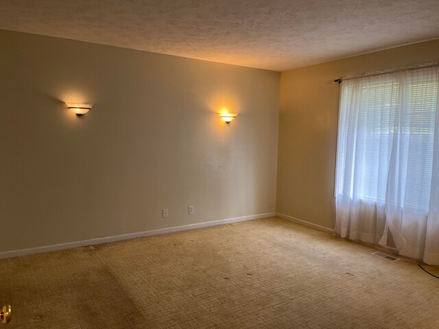 unfurnished room with visible vents, light carpet, a textured ceiling, and baseboards