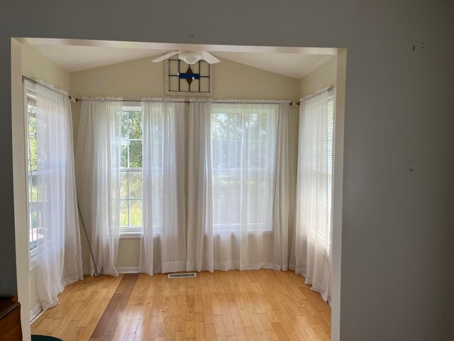 spare room featuring visible vents, plenty of natural light, light wood-style floors, and vaulted ceiling