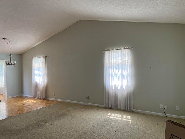 spare room featuring baseboards, vaulted ceiling, a textured ceiling, carpet flooring, and a notable chandelier