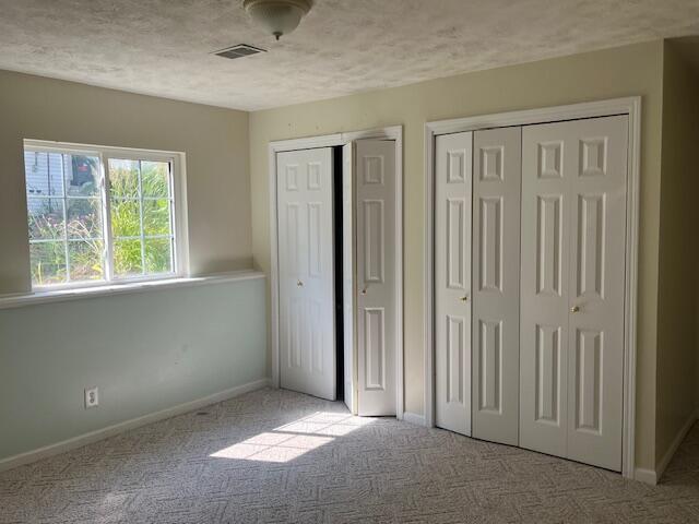 unfurnished bedroom featuring carpet, baseboards, visible vents, multiple closets, and a textured ceiling