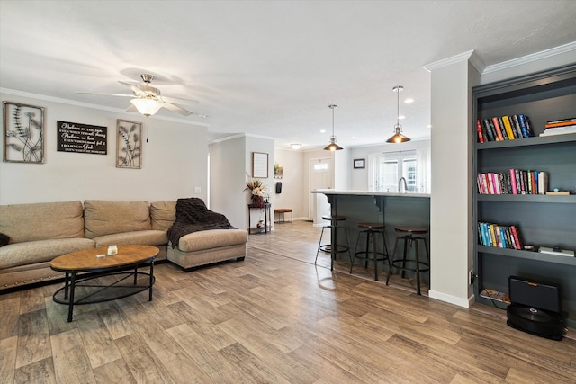 living room with light wood-type flooring, ornamental molding, built in shelves, ceiling fan, and sink