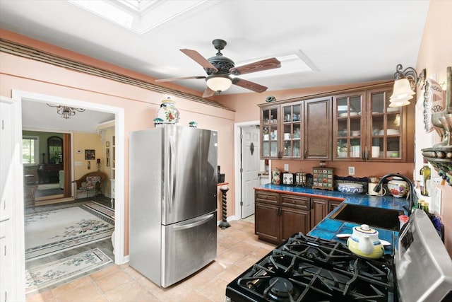 kitchen with dark brown cabinetry, sink, light tile patterned floors, black gas stove, and stainless steel refrigerator