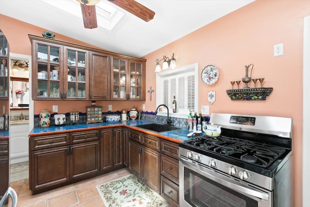 kitchen with gas stove, dark brown cabinetry, sink, vaulted ceiling with skylight, and light tile patterned flooring