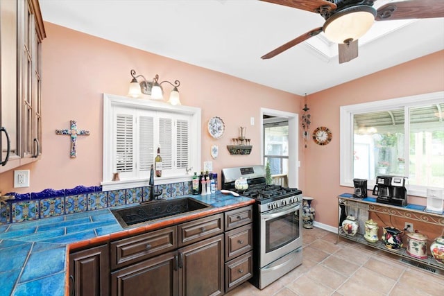 kitchen featuring ceiling fan, sink, stainless steel gas stove, lofted ceiling, and light tile patterned flooring