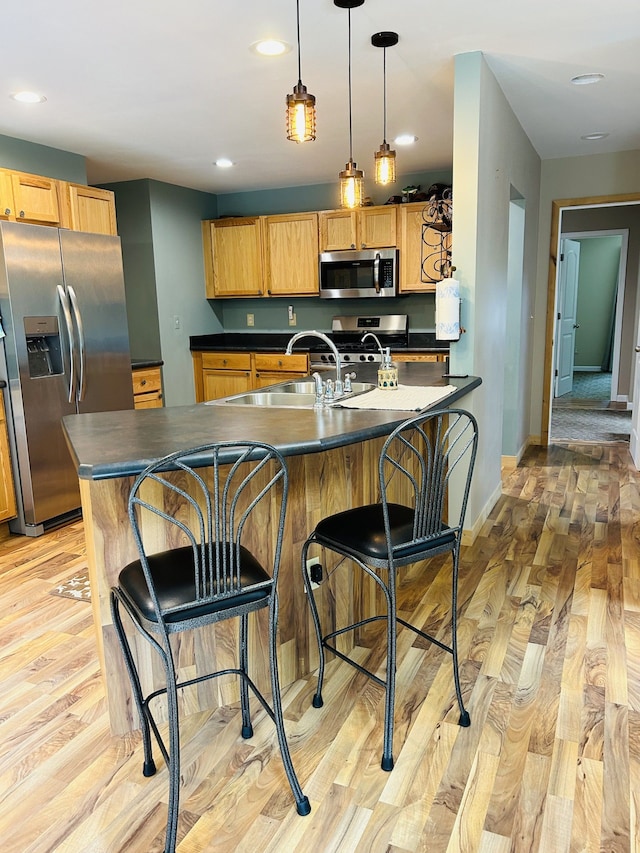 kitchen with sink, stainless steel appliances, decorative light fixtures, a breakfast bar area, and light wood-type flooring