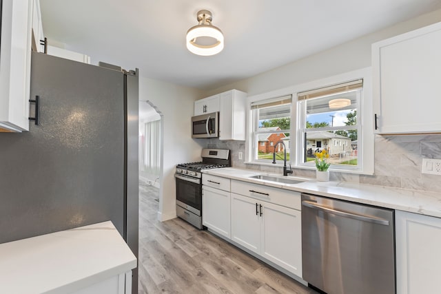 kitchen featuring decorative backsplash, stainless steel appliances, sink, white cabinets, and light hardwood / wood-style floors