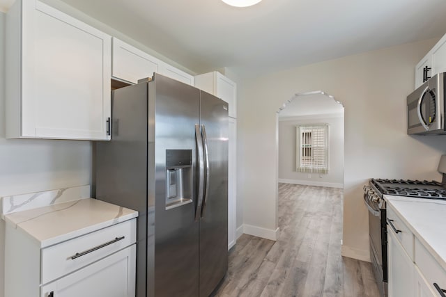 kitchen featuring light stone countertops, white cabinets, light hardwood / wood-style floors, and appliances with stainless steel finishes