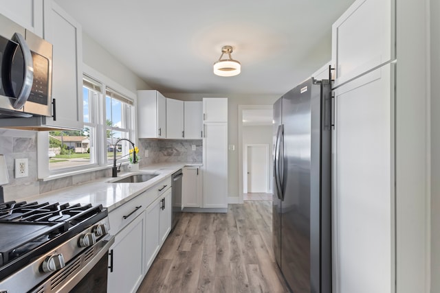 kitchen with appliances with stainless steel finishes, backsplash, sink, white cabinets, and light hardwood / wood-style floors