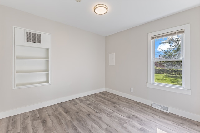 unfurnished room with built in shelves and light hardwood / wood-style floors