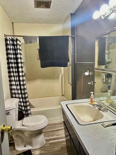 full bathroom with wood-type flooring, a textured ceiling, toilet, vanity, and shower / tub combo