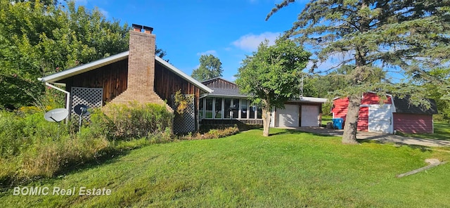 rear view of property featuring a lawn, a sunroom, and a garage