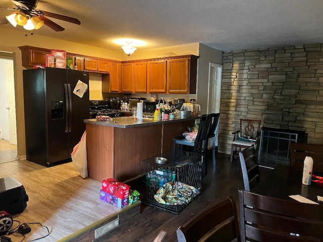 kitchen with black refrigerator with ice dispenser, light hardwood / wood-style flooring, ceiling fan, a textured ceiling, and kitchen peninsula