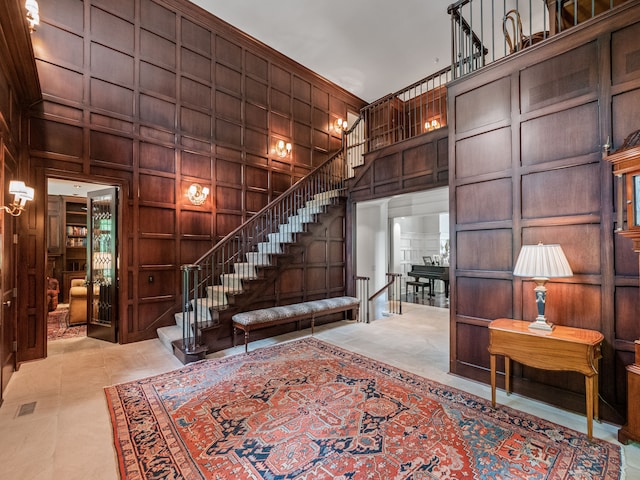 interior space with wood walls, a towering ceiling, and light tile patterned floors