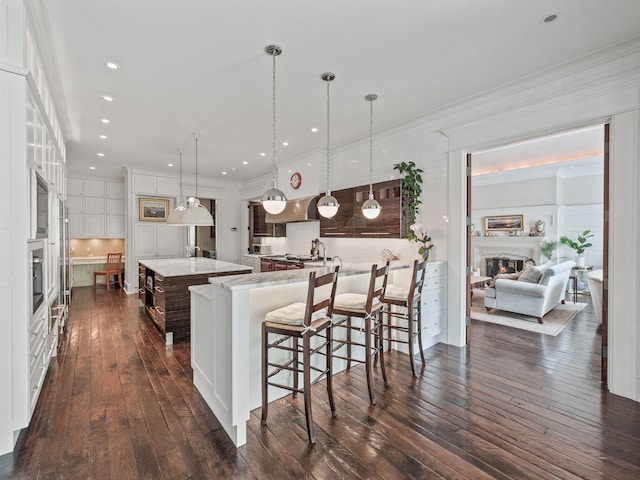 kitchen featuring white cabinetry, hanging light fixtures, dark hardwood / wood-style floors, a spacious island, and a kitchen bar