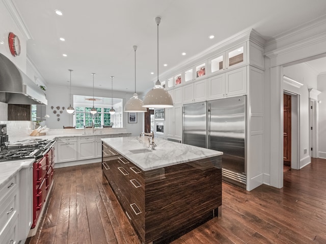 kitchen featuring dark hardwood / wood-style flooring, decorative light fixtures, stainless steel built in fridge, and an island with sink