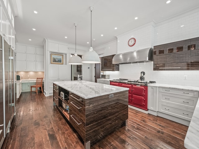 kitchen featuring dark hardwood / wood-style flooring, a center island with sink, decorative light fixtures, and wall chimney range hood