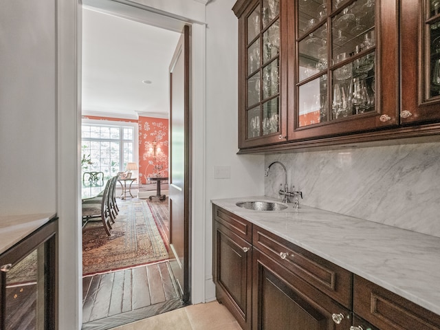 bar with light stone counters, beverage cooler, crown molding, sink, and light hardwood / wood-style floors