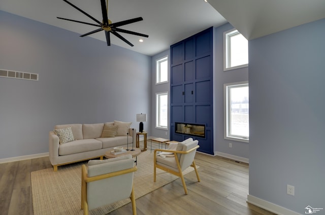 living room with a towering ceiling, a large fireplace, ceiling fan, and light wood-type flooring