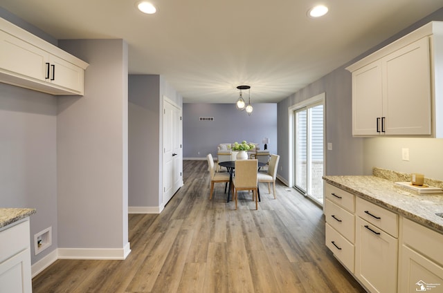 kitchen featuring light stone counters, hanging light fixtures, light hardwood / wood-style floors, and white cabinets