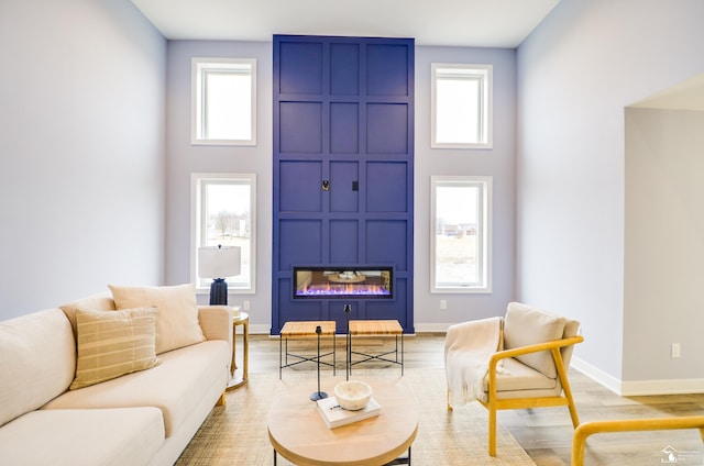 living room featuring a large fireplace, a healthy amount of sunlight, light hardwood / wood-style floors, and a towering ceiling