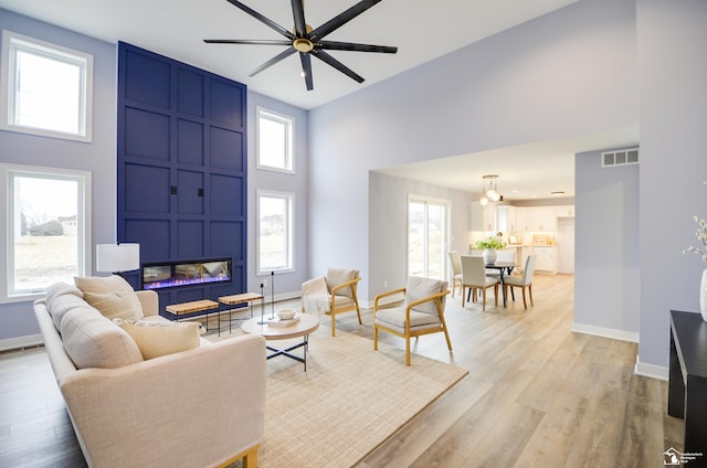 living room with light hardwood / wood-style floors, a large fireplace, ceiling fan, and a high ceiling