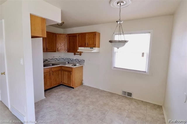 2439 Stieber St, Westland, MI 48186 - kitchen featuring a sink, brown cabinets, under cabinet range hood, light countertops, and hanging light fixtures