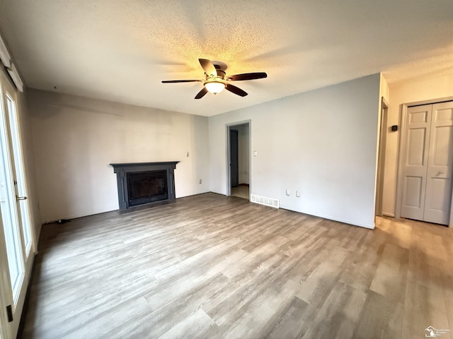 unfurnished living room with ceiling fan, light hardwood / wood-style floors, and a textured ceiling