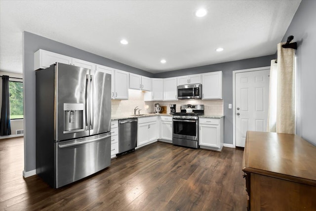 kitchen featuring appliances with stainless steel finishes, backsplash, light stone counters, dark wood-type flooring, and white cabinetry