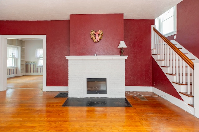 unfurnished living room with hardwood / wood-style floors, a healthy amount of sunlight, built in features, and a brick fireplace