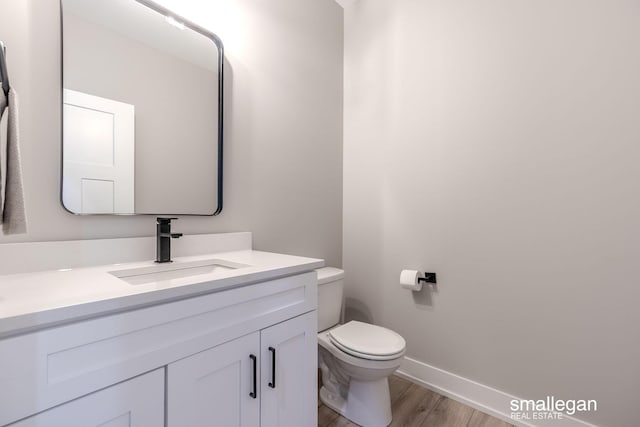 bathroom with baseboards, vanity, toilet, and wood finished floors