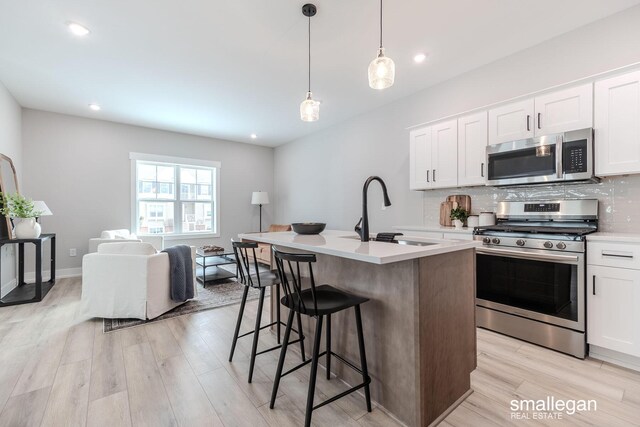 kitchen with a sink, stainless steel appliances, light countertops, light wood-type flooring, and backsplash