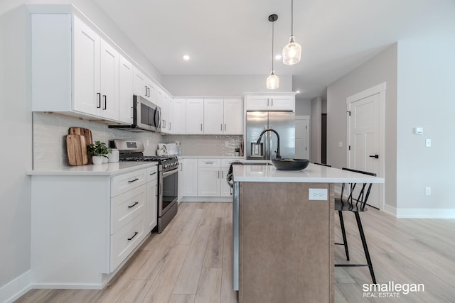 kitchen with stainless steel appliances, backsplash, light wood finished floors, a kitchen bar, and a center island with sink