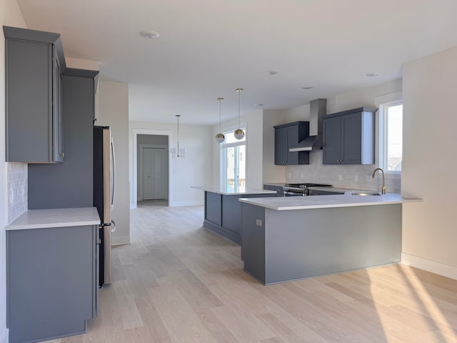 kitchen featuring decorative light fixtures, wall chimney range hood, stainless steel appliances, light hardwood / wood-style floors, and kitchen peninsula