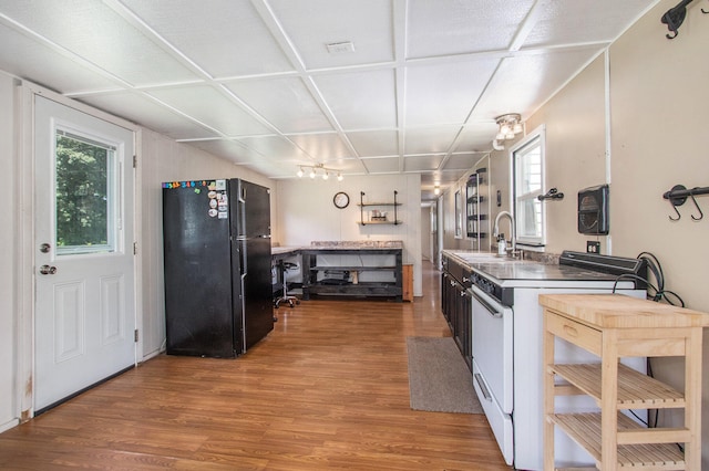 kitchen featuring hardwood / wood-style floors, black refrigerator, white range, and sink