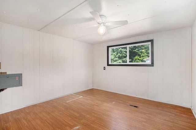 empty room with hardwood / wood-style flooring, ceiling fan, and wood walls