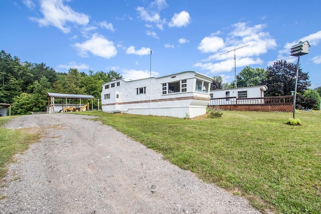 manufactured / mobile home featuring a wooden deck, a front yard, and a carport