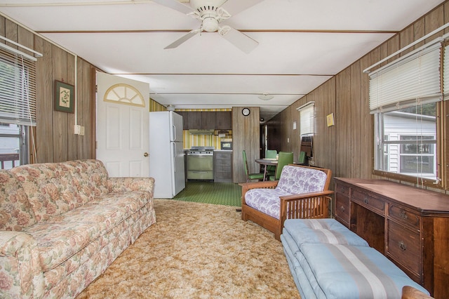 living room with carpet floors, ceiling fan, and wood walls