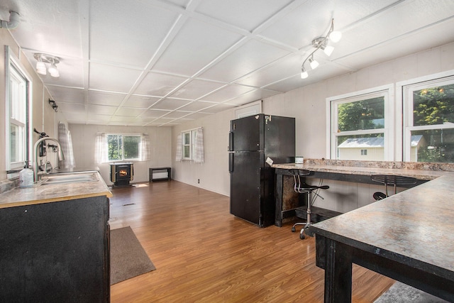 kitchen with a wood stove, coffered ceiling, black fridge, sink, and hardwood / wood-style flooring