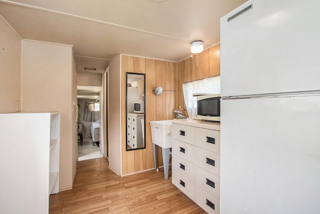 kitchen with wood walls, white refrigerator, and light wood-type flooring