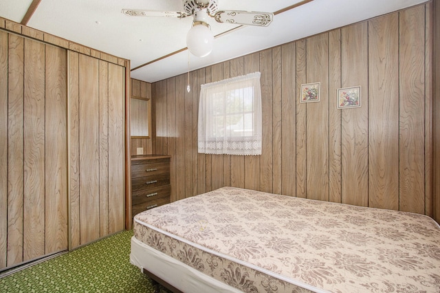 bedroom featuring carpet, a closet, ceiling fan, and wooden walls