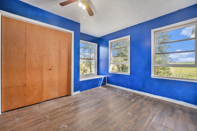 unfurnished bedroom featuring a closet, multiple windows, ceiling fan, and dark hardwood / wood-style flooring