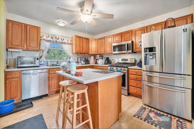 kitchen featuring ceiling fan, stainless steel appliances, light hardwood / wood-style floors, a kitchen bar, and a kitchen island