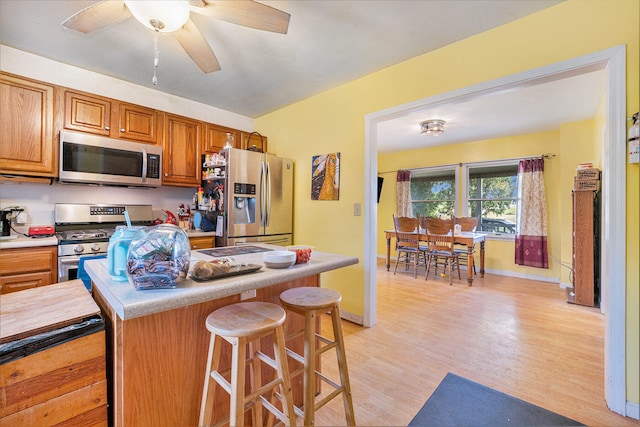 kitchen with a kitchen breakfast bar, ceiling fan, light hardwood / wood-style floors, and appliances with stainless steel finishes