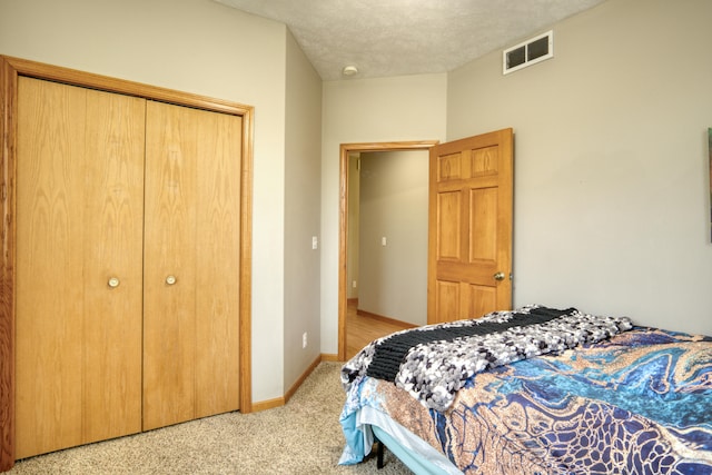 bedroom with a textured ceiling, light colored carpet, and a closet