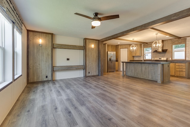 kitchen with a kitchen bar, appliances with stainless steel finishes, ceiling fan with notable chandelier, pendant lighting, and light hardwood / wood-style flooring